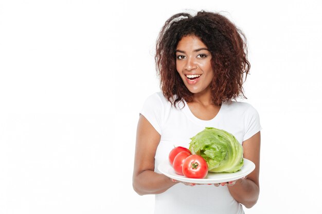 Heureuse jeune femme africaine tenant des légumes.