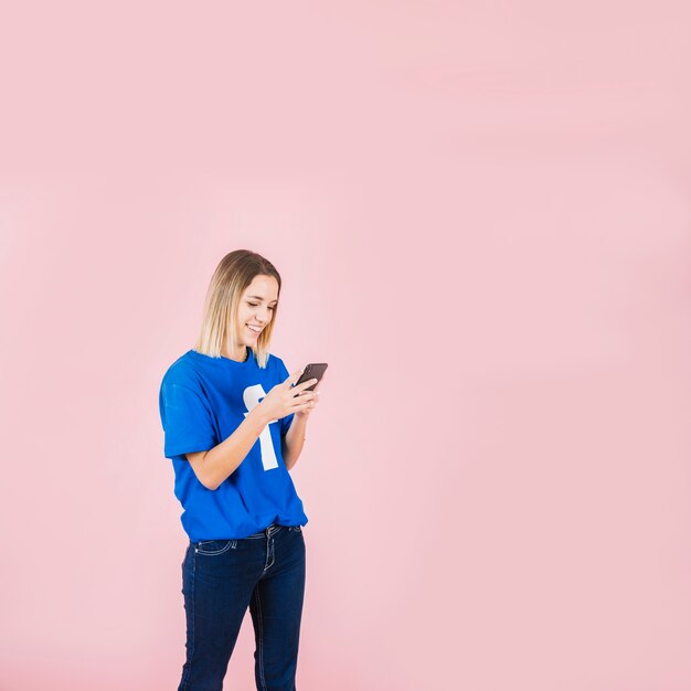 Heureuse jeune femme à l&#39;aide de téléphone portable sur fond rose