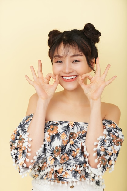 Heureuse jeune femme asiatique qui pose en studio avec sourire ouvert et gestes de la main drôle