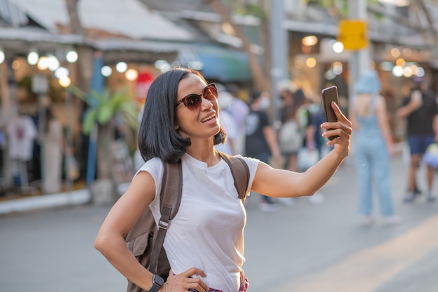 Heureuse jeune femme asiatique de voyage à l'aide de téléphone portable et se détendre dans la rue.