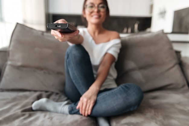 Photo gratuite heureuse jeune femme assise sur le canapé à la maison regarder la télévision.