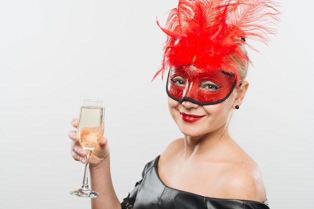 Photo gratuite heureuse jeune femme au masque avec des plumes rouges, tenant le verre