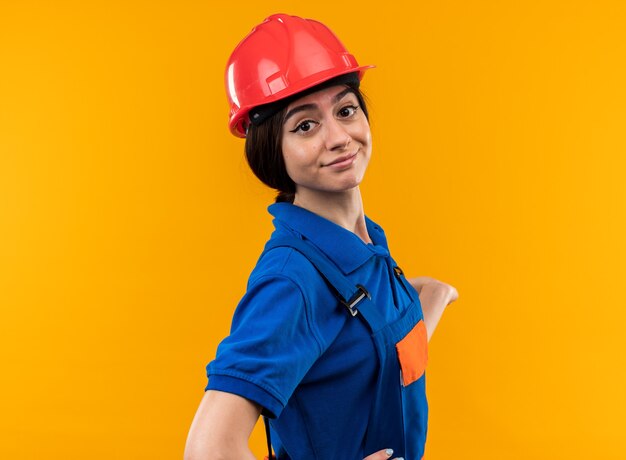 Heureuse jeune femme de construction en uniforme isolée sur un mur jaune