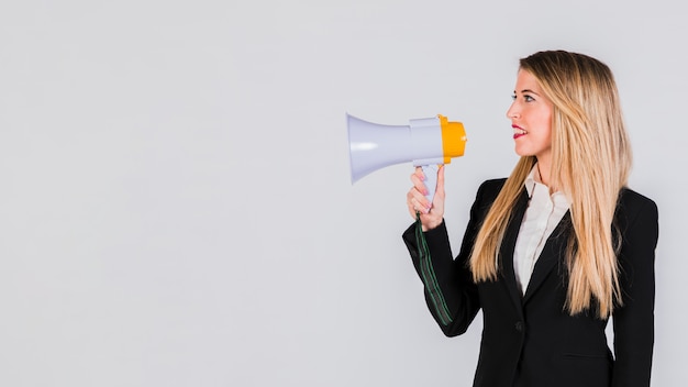 Heureuse jeune femme crier sur un mégaphone sur fond gris