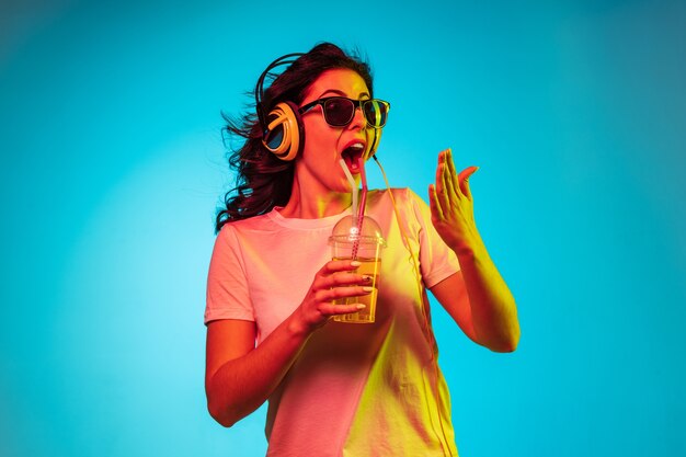 Heureuse jeune femme danse et souriant dans les écouteurs sur studio néon bleu branché