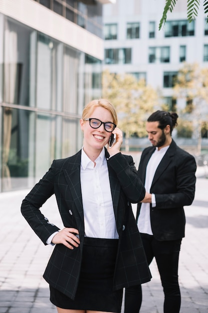 Photo gratuite heureuse jeune femme debout devant son collègue parlant au téléphone