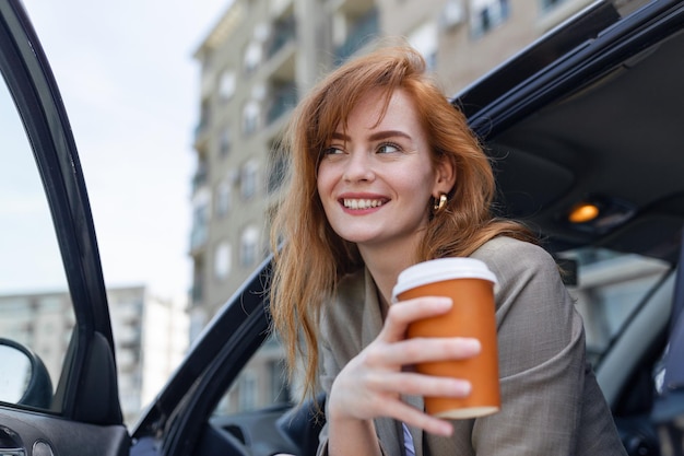 Photo gratuite heureuse jeune femme avec du café ayant un frein dans sa voiture vue latérale d'une femme avec du café à emporter jeune femme buvant du café dans sa voiture