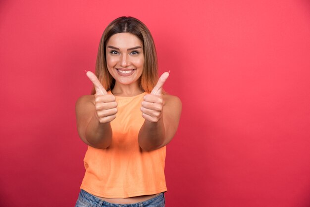 Heureuse jeune femme faisant les pouces vers le haut sur le mur rouge.