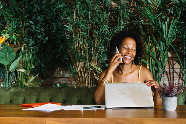 Heureuse jeune femme fermant l&#39;ordinateur portable tout en parlant au téléphone portable