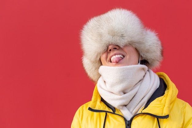 Heureuse jeune femme sur le fond d'un mur rouge dans des vêtements chauds sur une journée ensoleillée d'hiver sourit avec un sourire blanc comme neige