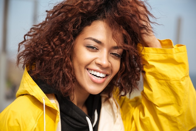 Heureuse jeune femme frisée africaine portant un manteau jaune