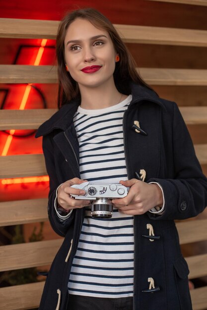 Heureuse jeune femme hipster tient un appareil photo rétro. S'amuser dans la ville avec un appareil photo, photo de voyage du photographe.