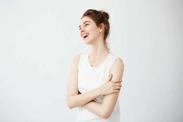 Heureuse jeune femme joyeuse avec chignon souriant en riant. Les bras croisés.