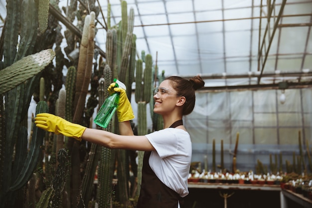 Photo gratuite heureuse jeune femme à lunettes debout dans une serre près des plantes.