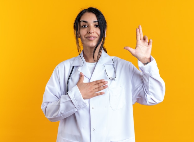 Photo gratuite heureuse jeune femme médecin portant une robe médicale avec stéthoscope montrant un geste de pistolet isolé sur un mur jaune