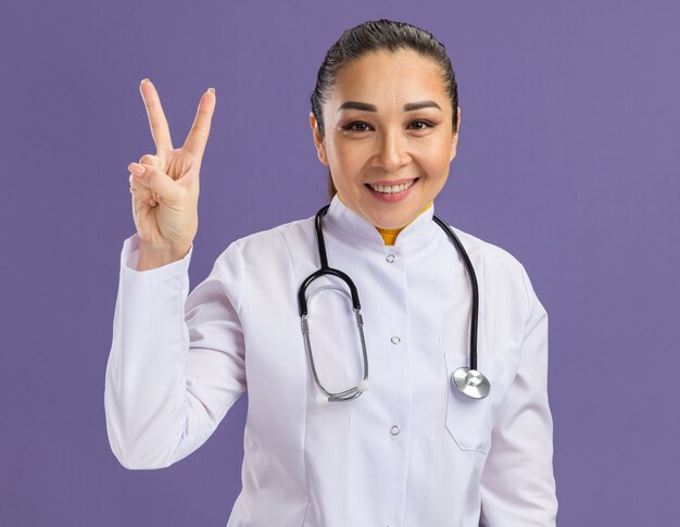 Heureuse jeune femme médecin souriant montrant le signe v