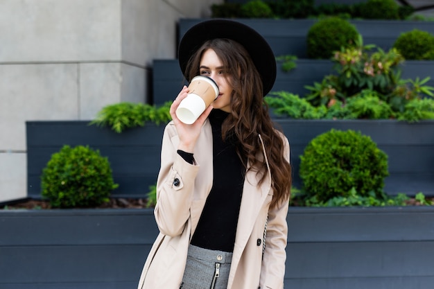 Heureuse jeune femme à la mode, boire du café à emporter et marcher après le shopping dans une ville urbaine.