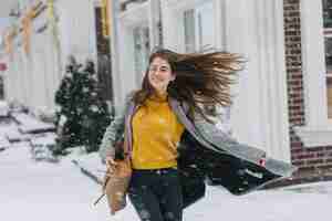 Photo gratuite heureuse jeune femme à la mode profitant des chutes de neige sur la rue en ville. longs cheveux bruns, temps de neige, émotions excitées s'amusant, souriant. ambiance de noël, nouvel an à venir, vrai bonheur.