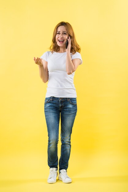 Heureuse jeune femme parle au téléphone portable sur fond jaune