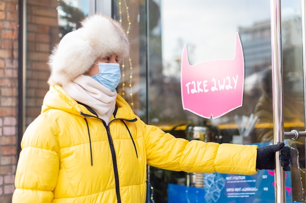 Heureuse jeune femme à la porte du restaurant par une froide journée d'hiver, lettrage, plats à emporter.