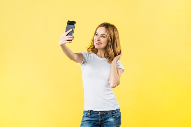 Heureuse jeune femme prenant selfie sur portable sur fond jaune