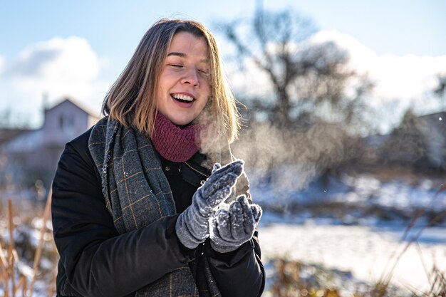 Heureuse jeune femme en promenade en hiver avec de la neige dans les mains