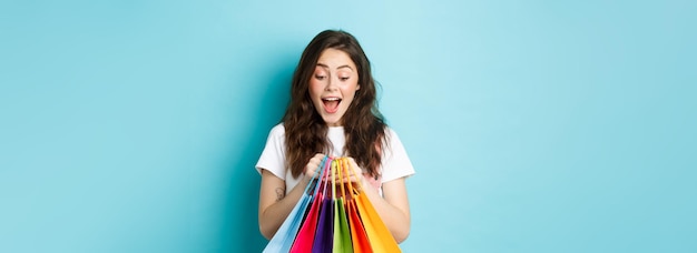 Photo gratuite heureuse jeune femme regardant ses sacs de shopping avec enthousiasme en achetant avec des réductions dans les magasins standi