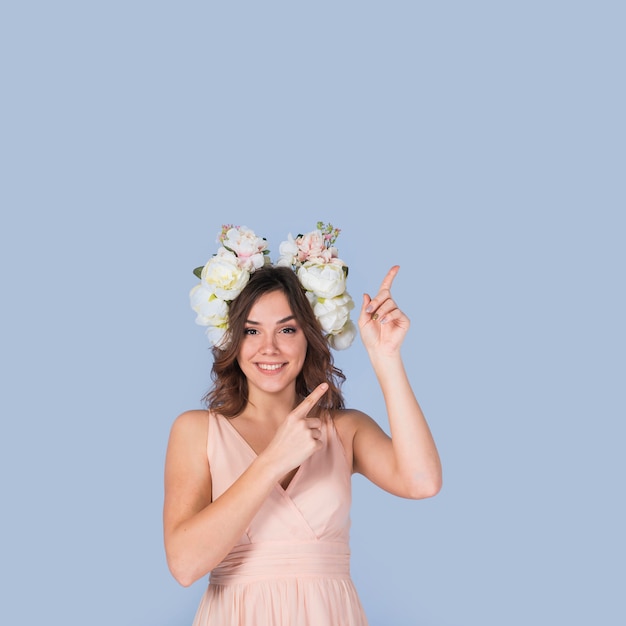 Heureuse jeune femme en robe avec une couronne blanche pointant à l&#39;étage