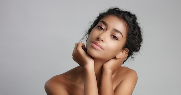 Heureuse jeune femme sereine avec une belle peau d'olive et des cheveux bouclés, une peau idéale et des yeux bruns en studio