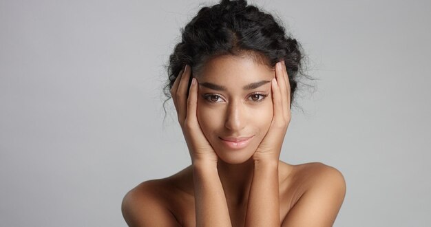 Heureuse jeune femme sereine avec une belle peau d'olive et des cheveux bouclés, une peau idéale et des yeux bruns en studio