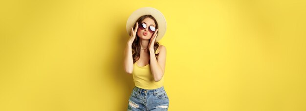 Heureuse jeune femme sexy en vacances portant des lunettes de soleil chapeau de paille riant et souriant debout sur y