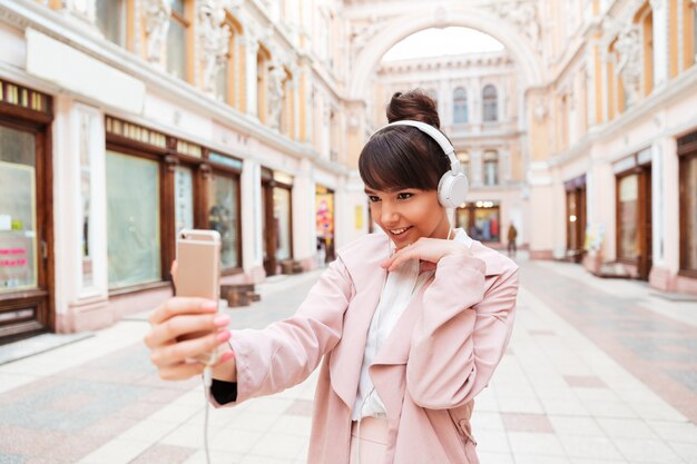 Heureuse jeune femme souriante dans les écouteurs faisant selfie