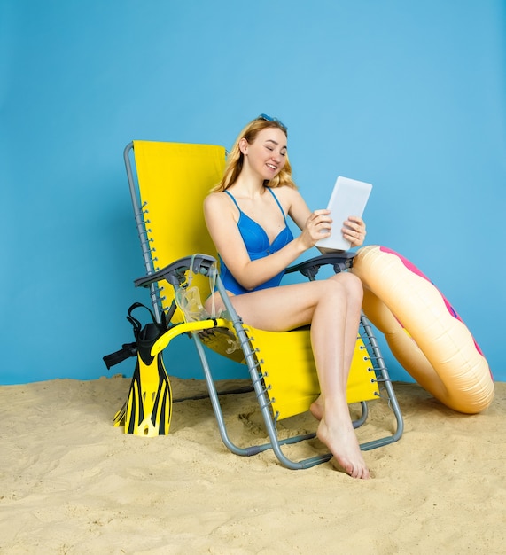 Heureuse jeune femme avec tablette prend selfie ou vlog sur les voyages sur fond bleu studio. Concept d'émotions humaines, expression faciale, vacances d'été, week-end. L'été, la mer, l'océan, l'alcool.