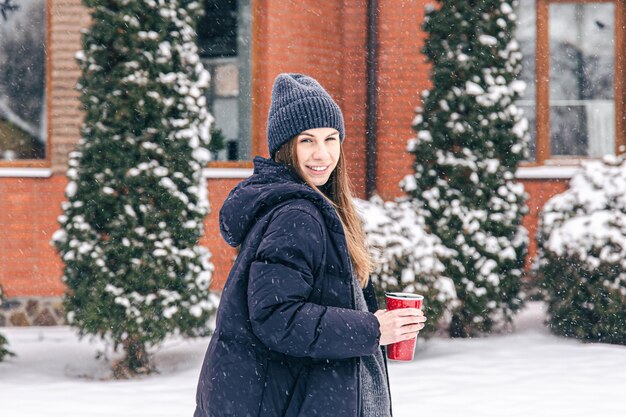 Heureuse jeune femme avec tasse thermo par temps de neige