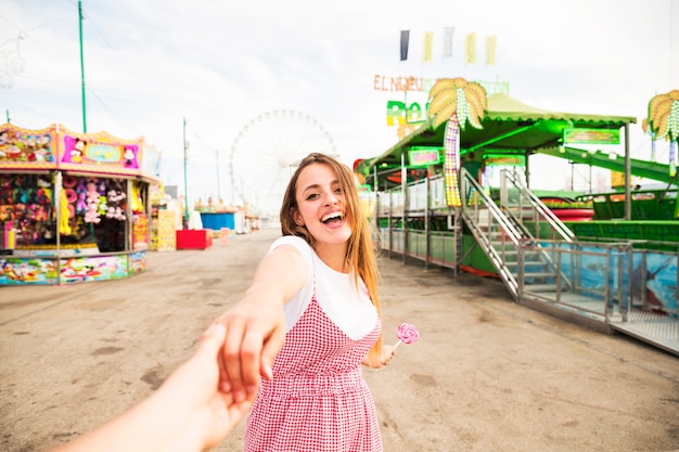 Heureuse jeune femme tenant la main de son petit ami au parc d&#39;attractions