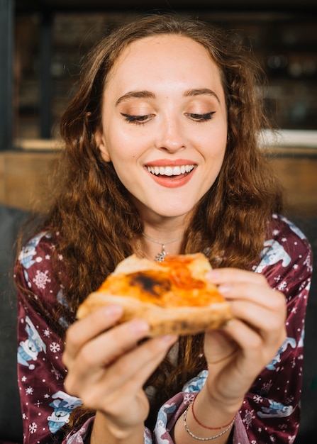 Heureuse jeune femme tenant une tranche de pizza