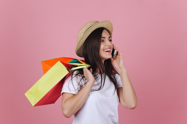 Heureuse jeune femme utilise son téléphone posant avec des sacs à provisions colorés dans le studio