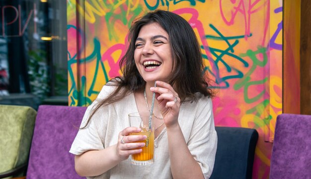 Heureuse jeune femme avec un verre de limonade contre un mur peint lumineux