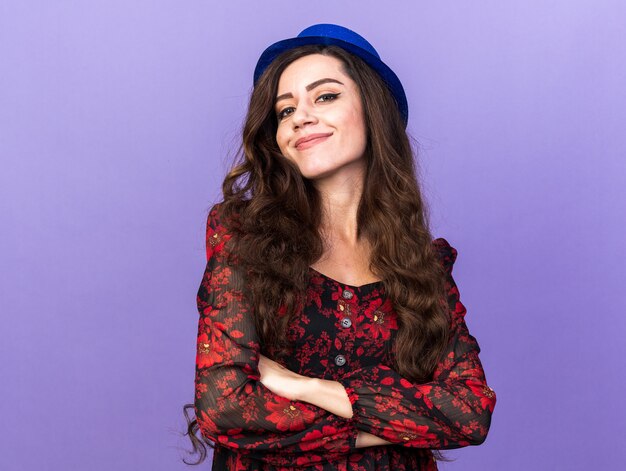 Heureuse jeune fêtarde portant un chapeau de fête debout avec une posture fermée isolée sur un mur violet avec espace de copie
