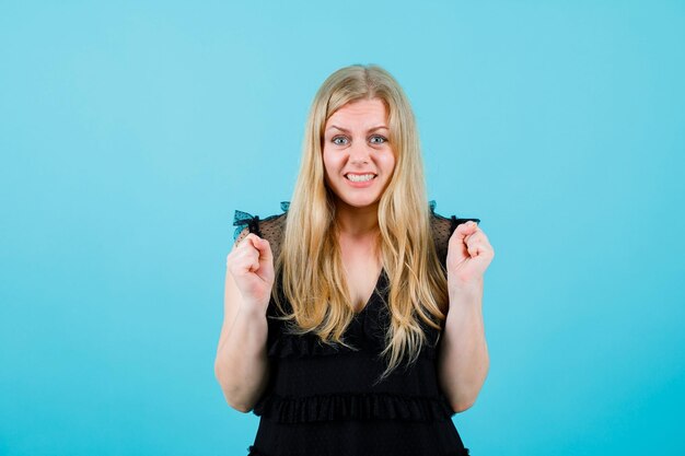 Heureuse jeune fille blonde lève les poings sur fond bleu