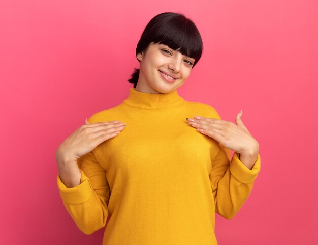 Heureuse jeune fille caucasienne brune met les mains sur la poitrine