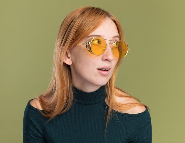 Heureuse jeune fille rousse au gingembre avec des taches de rousseur dans des lunettes de soleil regardant de côté