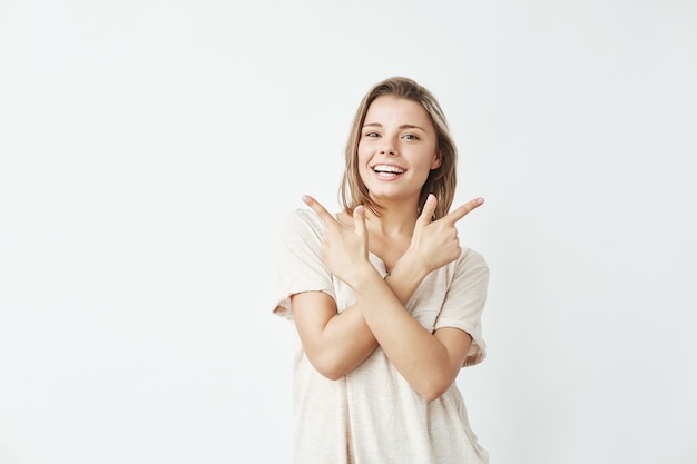 Heureuse jeune fille sincère, pointant les doigts vers le haut en souriant.