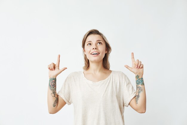 Heureuse jeune fille sincère, pointant les doigts vers le haut en souriant.