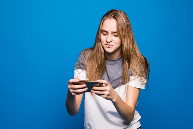 Heureuse jeune fille souriante avec téléphone portable lit un message devant un fond bleu