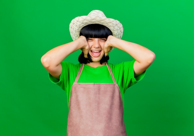 Heureuse jeune jardinière en uniforme portant un chapeau de jardinage tient la tête isolée