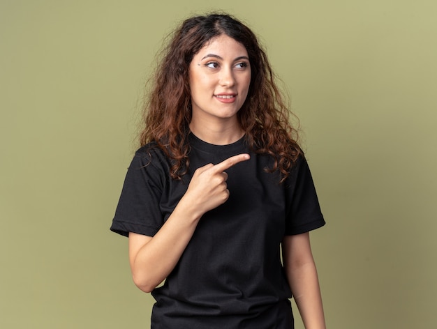 Heureuse jeune jolie femme regardant et pointant sur le côté isolé sur un mur vert olive avec espace pour copie