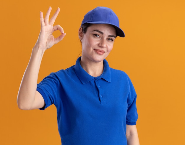 Heureuse jeune livreuse en uniforme et casquette faisant signe ok