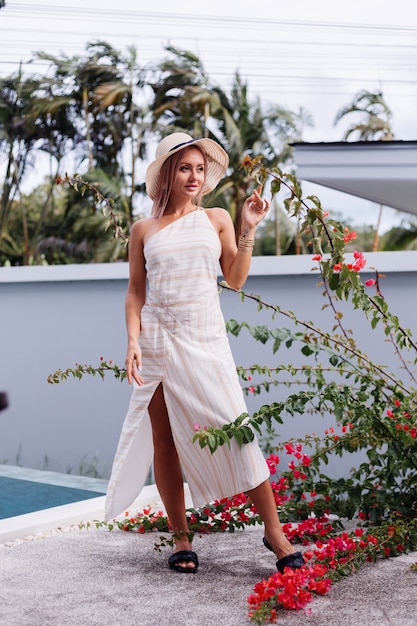 Photo gratuite heureuse jolie femme caucasienne romantique en été élégante robe blanche dos ouvert, chapeau de paille