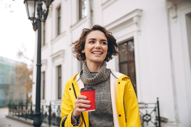 Heureuse jolie jeune femme buvant du café. En regardant de côté.